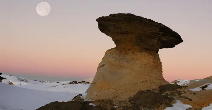 Rock formation in Bisti Badlands snowscape and full moon